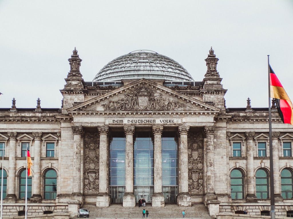 Photo by Niki Nagy Front view of the historic Reichstag Building in Berlin, Germany, featuring prominent German flags.