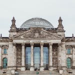Front view of the historic Reichstag Building in Berlin, Germany, featuring prominent German flags.