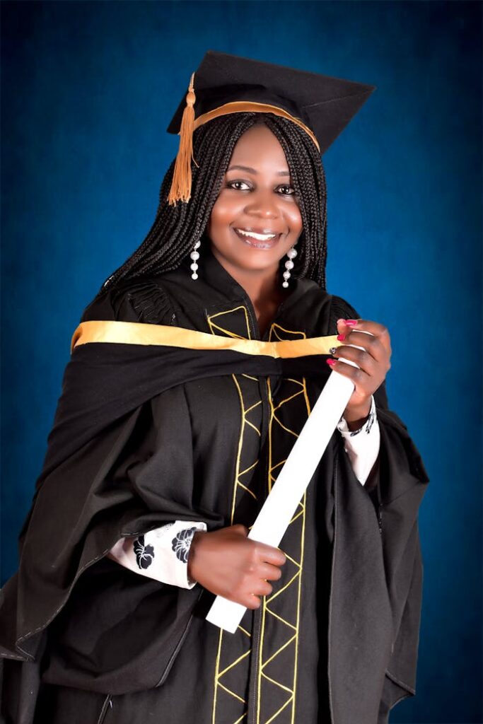 pexels-photo-8972641 Smiling woman in graduation gown posing with diploma in studio setting with blue background.
