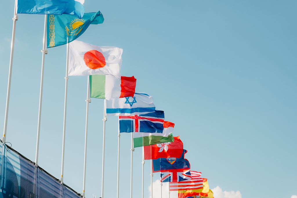 A row of international flags waving under a clear blue sky in Paris, France.