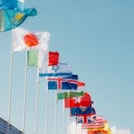 A row of international flags waving under a clear blue sky in Paris, France.