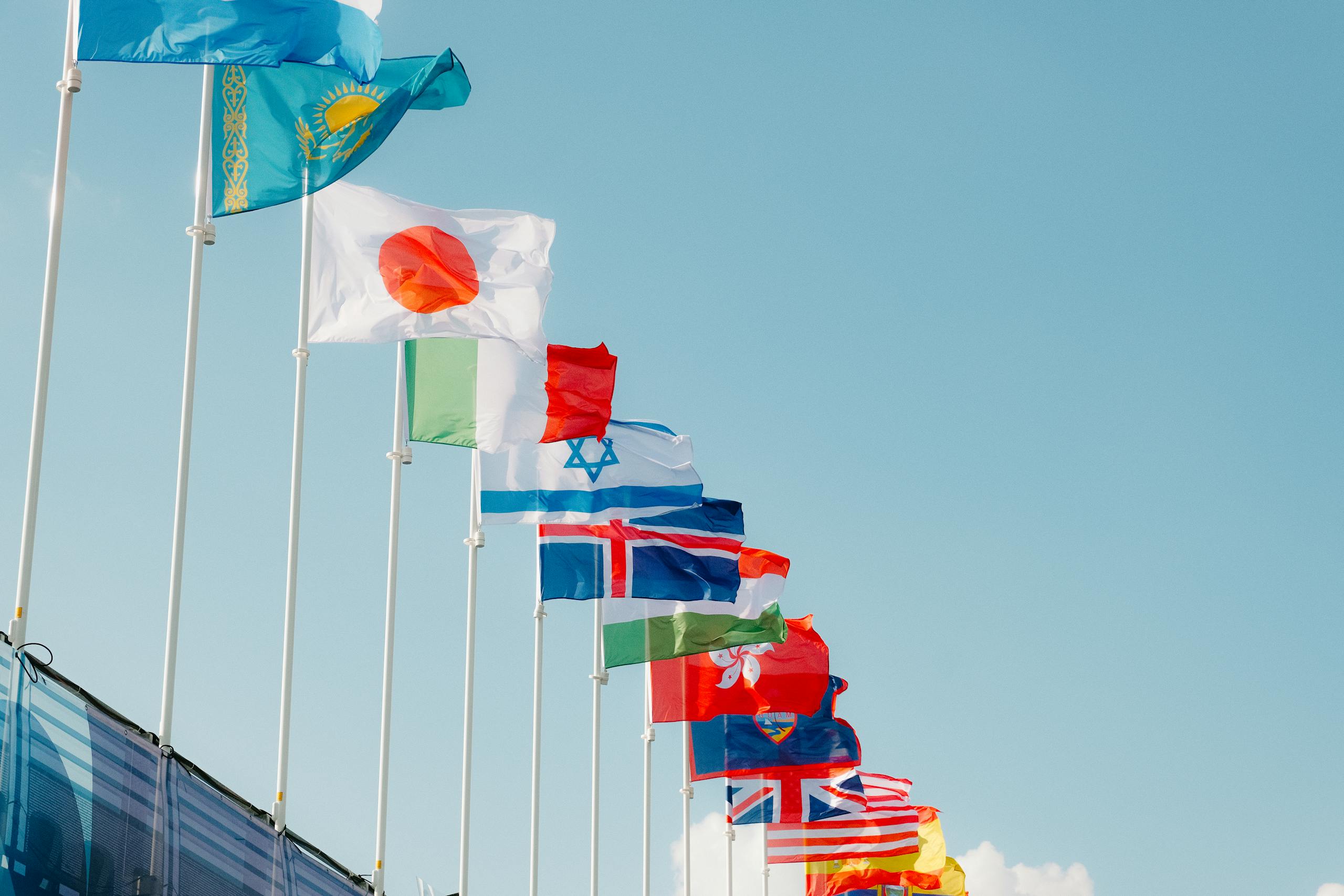 A row of international flags waving under a clear blue sky in Paris, France.